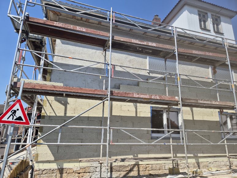 Fassade eines Altbaus mit Gerüst und freigelegter Wandfläche während der Sanierung